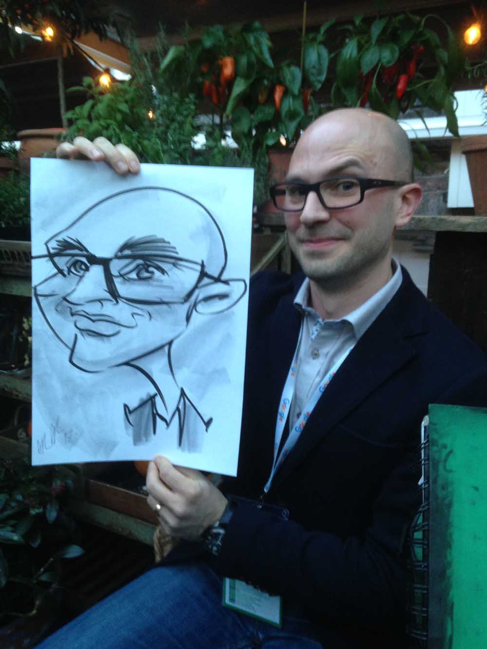 Man with glasses holding caricature by Allan Cavanagh