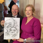 Man in suit and woman in heather mauve dress holding black and white caricature drawing, both laughing