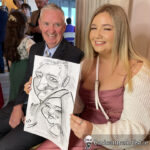 Father and daughter seated and laughing, holding a caricature by award-winning caricature artist Allan Cavanagh